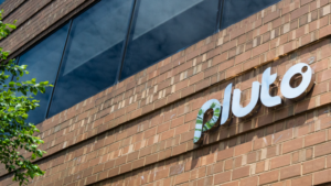 Exterior of a brick building with a modern sign that reads 'Pluto' near a glass window and a tree branch in the foreground.