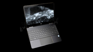 A photorealistic CGI rendering of an HP Spectre laptop, floating against a dark background with intricate lighting and reflections. The screen displays a high-contrast, abstract black-and-white visual, enhancing the futuristic look.