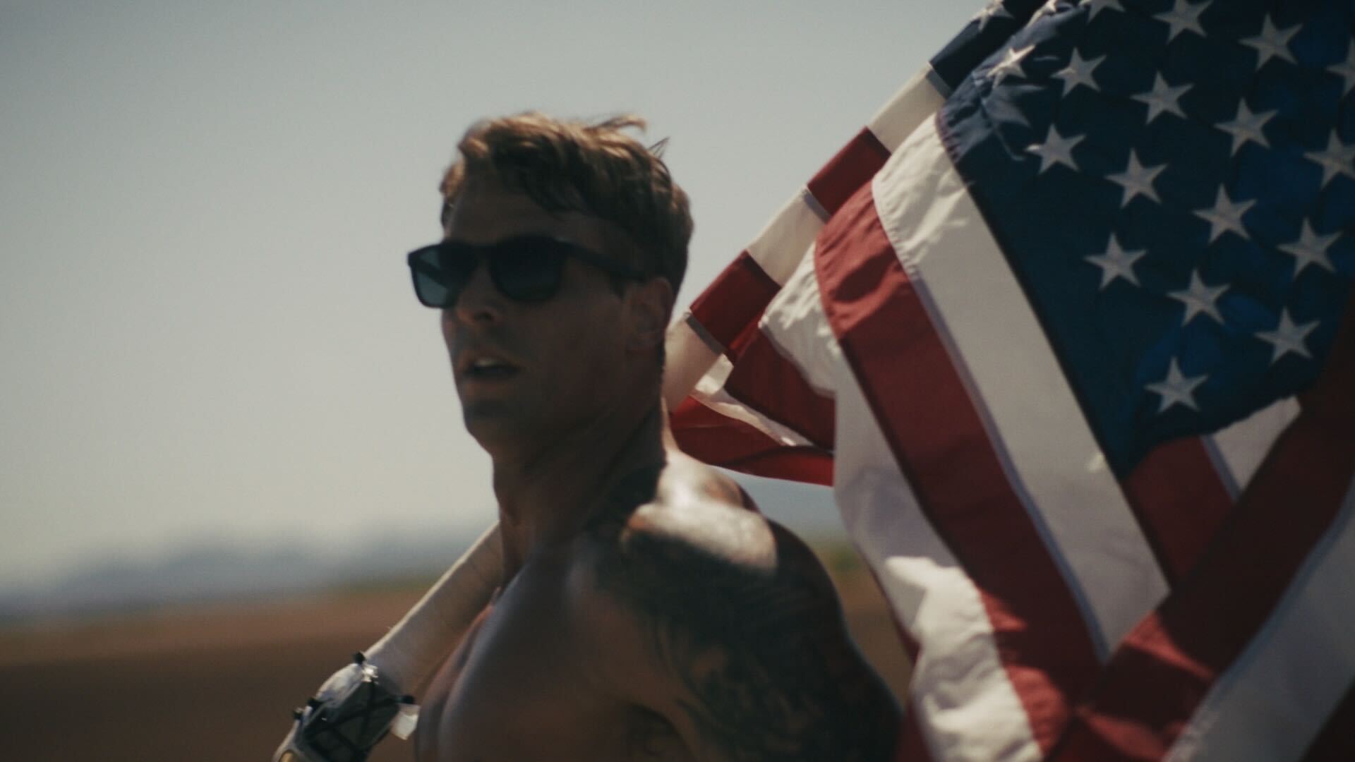 Shirtless man wearing sunglasses runs with an American flag during the Old Glory Ultra Relay across the United States